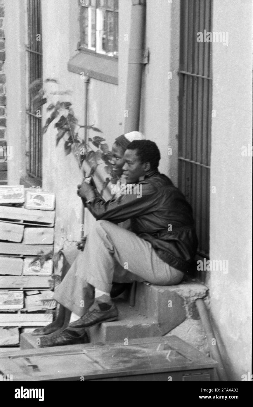 Lavoratori del negozio che fanno una pausa seduti sul gradino posteriore del negozio ascoltando la radio a transistor, Johannesburg Gauteng, Sud Africa, 1985. Dalla collezione - Sud Africa anni '1980 - Archivio fotografico Don Minnaar Foto Stock