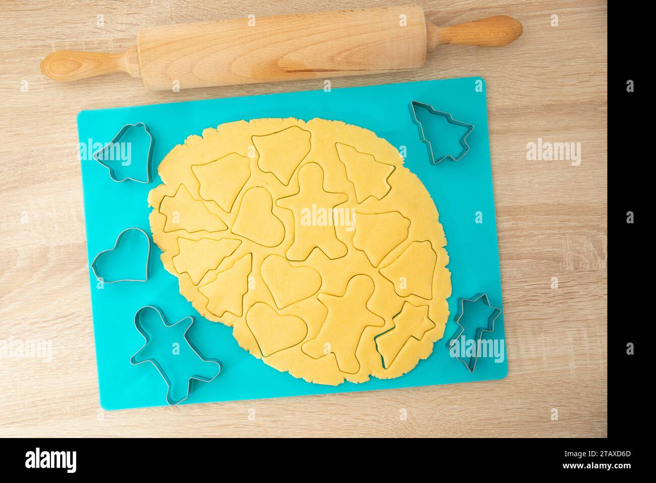 Cuocere i biscotti con un matterello e un taglierine su una base turchese su uno sfondo di legno Foto Stock