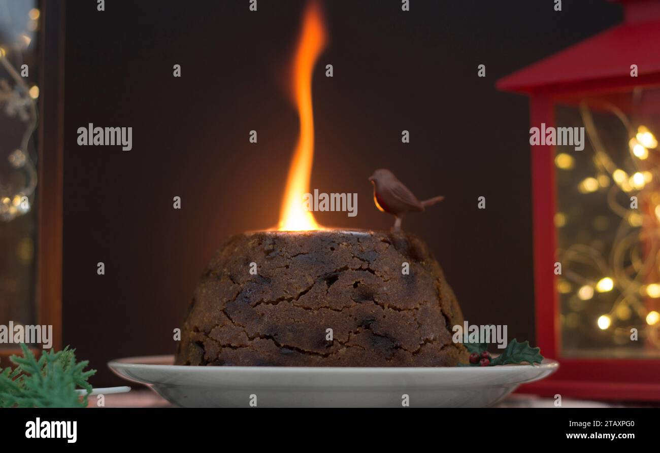 Fiamma budino di Natale tradizionale con brandy in cima guardato da un curioso robin ornamentale Foto Stock