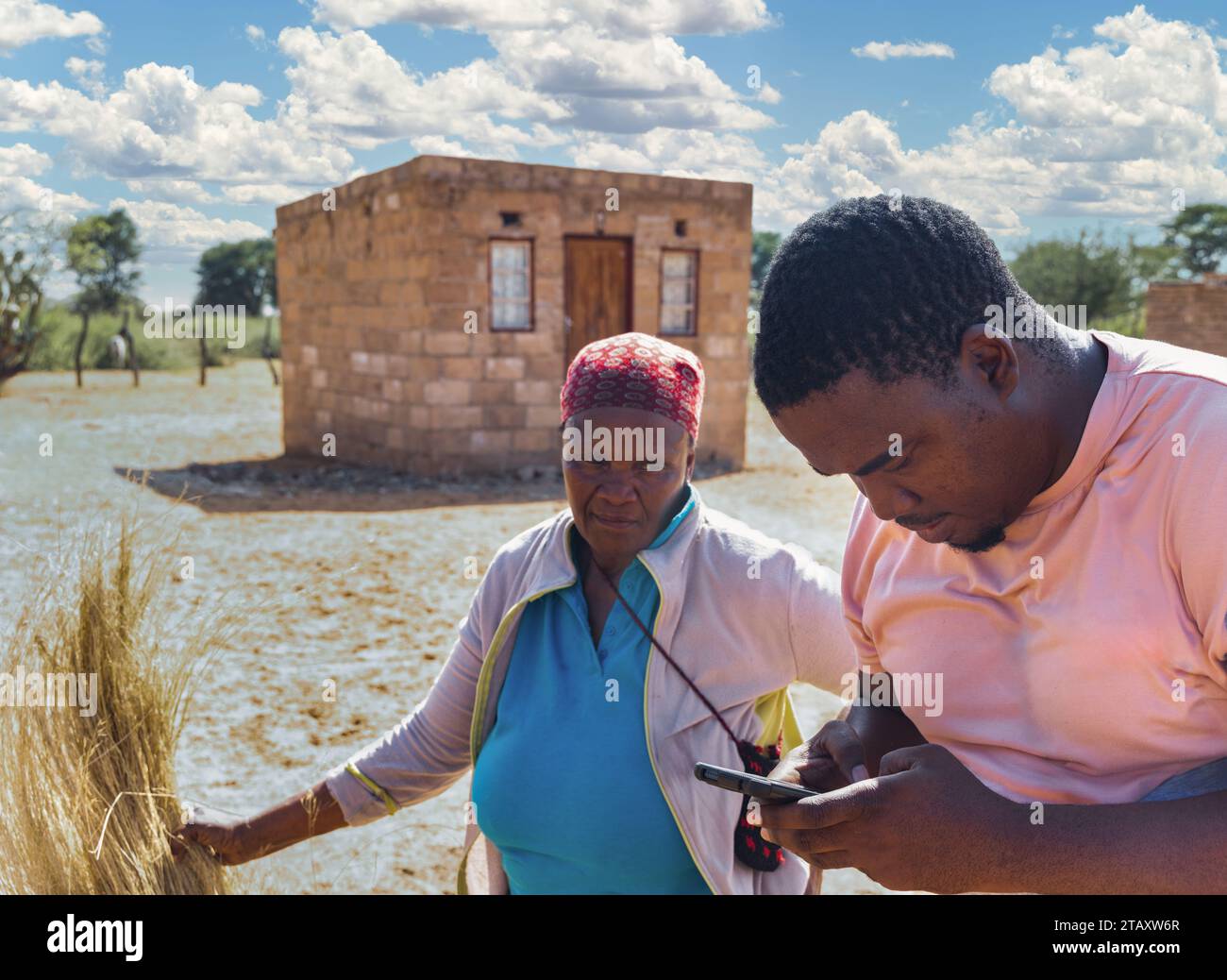 villaggio africano, vecchia donna che si apre davanti alla casa con un lavoratore di ong al telefono Foto Stock