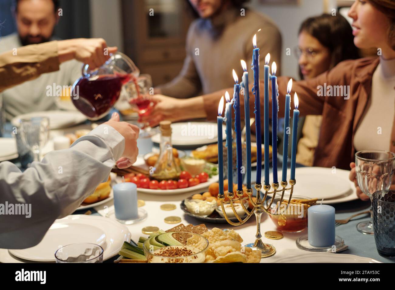 Concentrati sulle candele a fuoco blu sul candelabro menorah in piedi sul tavolo servito con cibo e bevande fatti in casa durante la cena di famiglia Hanukkah Foto Stock