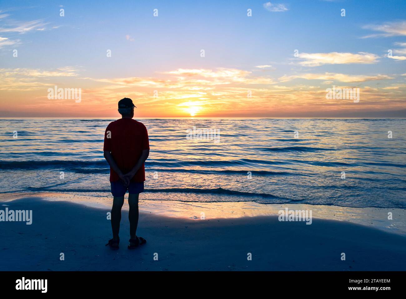 Un uomo anziano da solo sulla spiaggia al tramonto. Concetto di viaggio in solitaria, solitudine e isolamento. Foto Stock