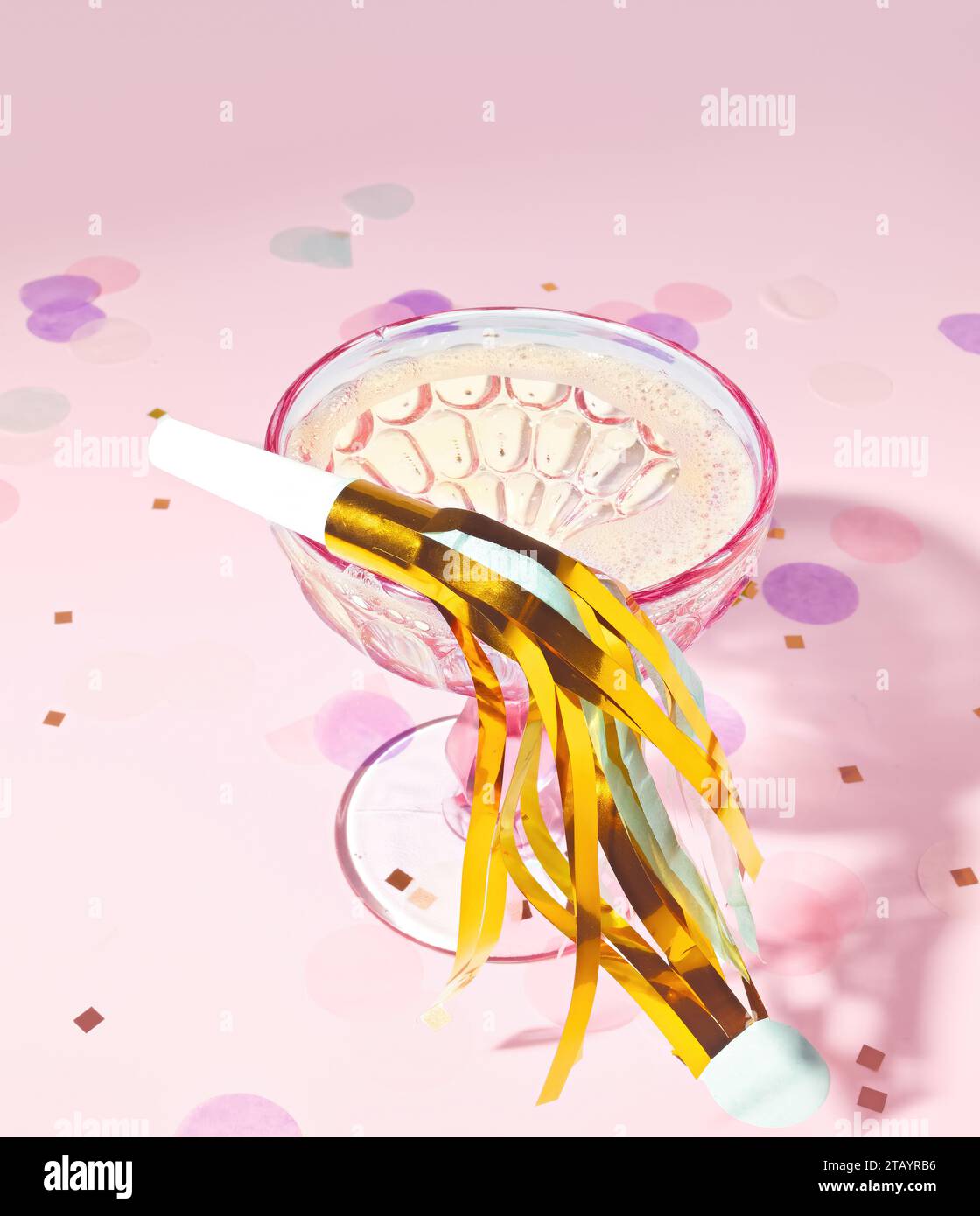 Party Horn con Gold Tinsel seduto su un celebrativo bicchiere di champagne e Confetti su un iridescente sfondo di Tinsel Party Scene in un sognante Colo pastello Foto Stock