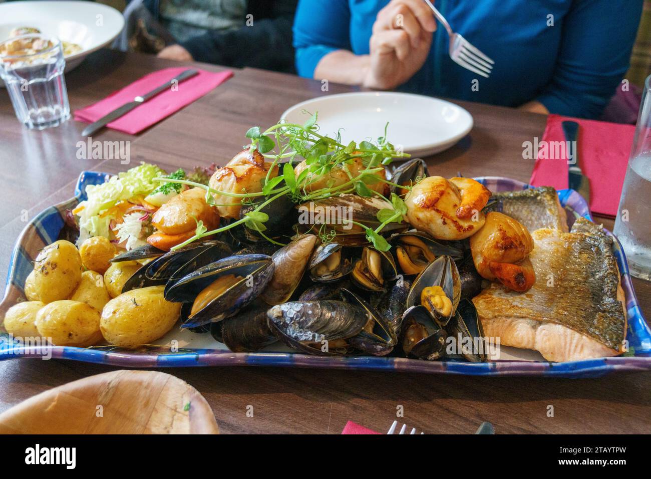 Enorme piatto di pesce con pesce, cozze e capesante. Un bravo commensale tiene un forchetta sullo sfondo. Foto Stock