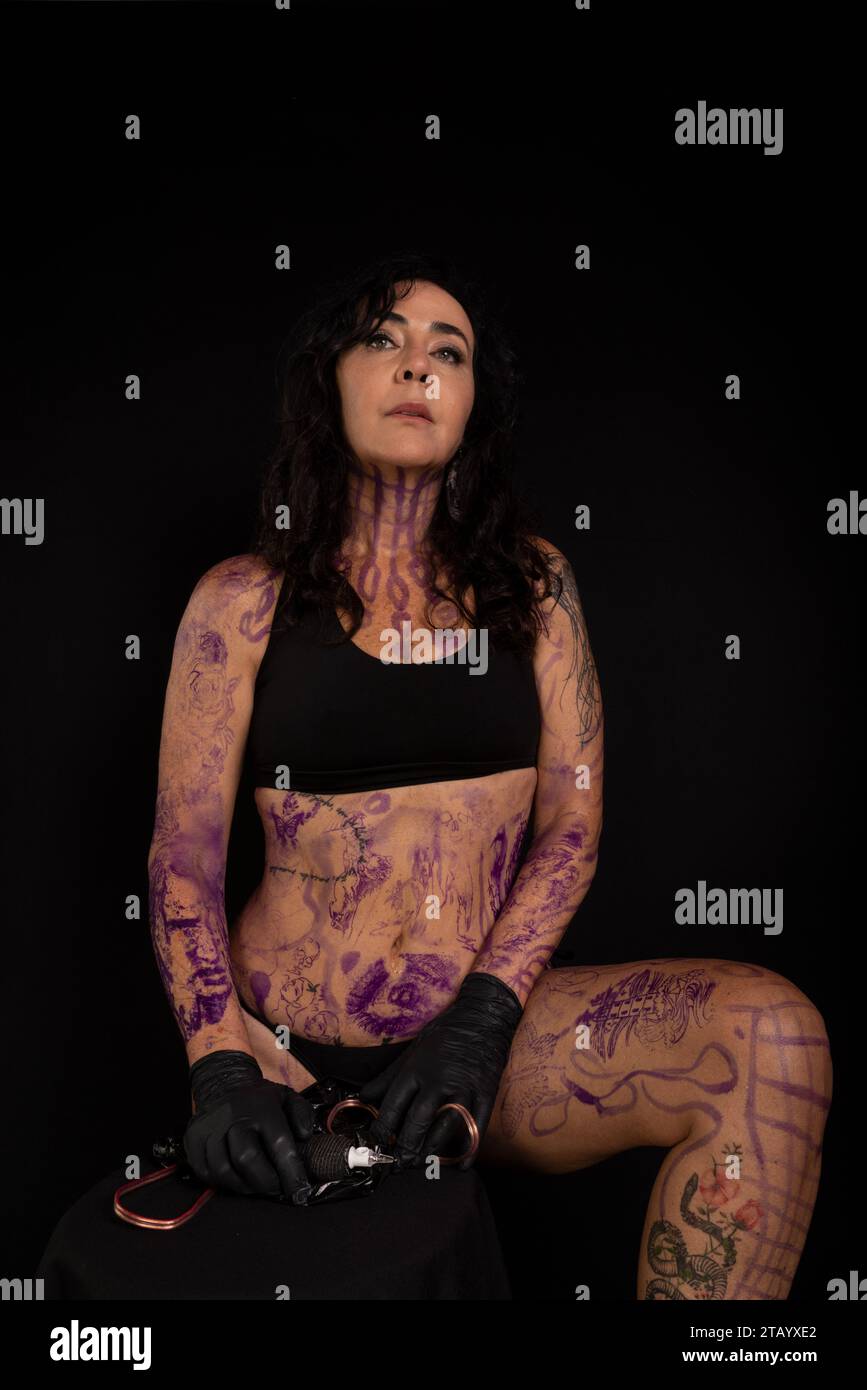 Bellissimo artista che tiene in mano la macchina del tatuaggio che guarda la fotocamera su sfondo nero Foto Stock