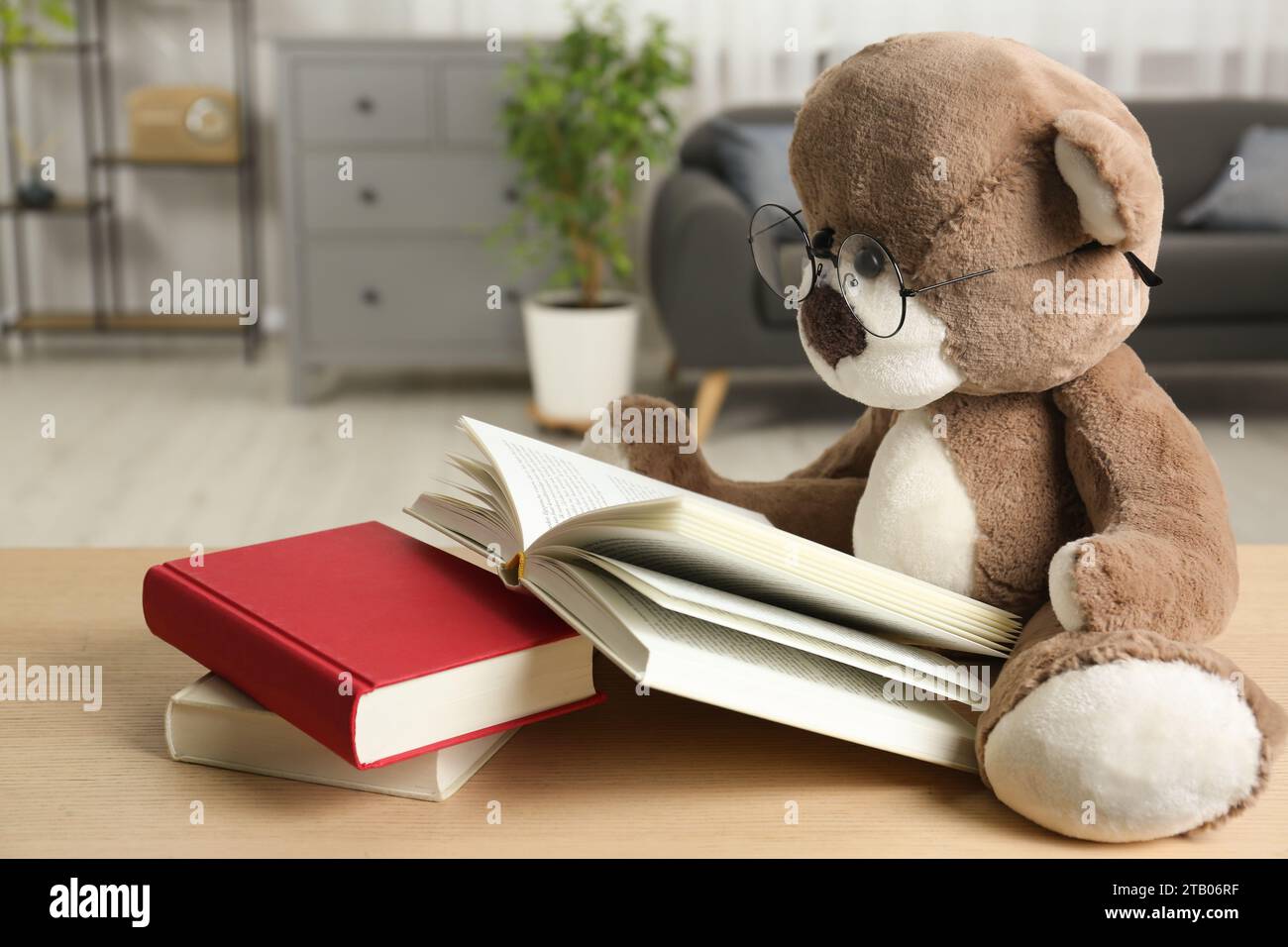 Orsacchiotto con occhiali e libro aperto su un tavolo di legno in camera, primo piano Foto Stock