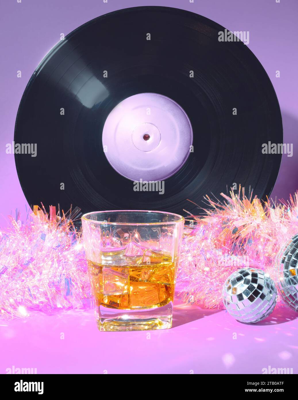 Un bicchiere di Scotch Whiskey, Un disco vinilico, palle a specchio e Tinsel natalizio olografico su sfondo rosa e viola pastello Foto Stock
