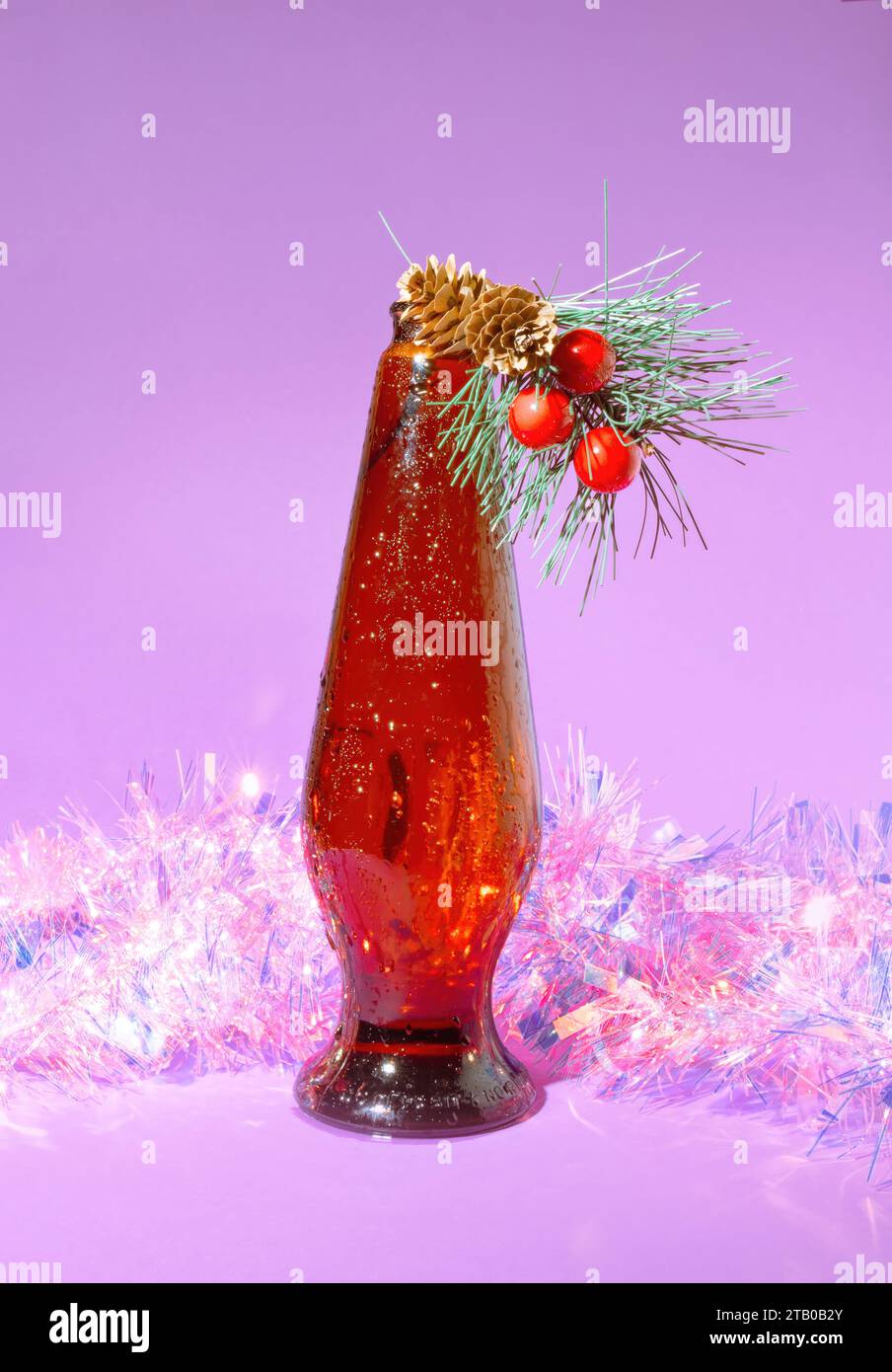 Una bottiglia d'ala rosa rétro di birra marrone con pino natalizio natalizio e decorazioni olografiche, iridescenti in tinsel pastello con Backgrou viola pastello pastello Foto Stock