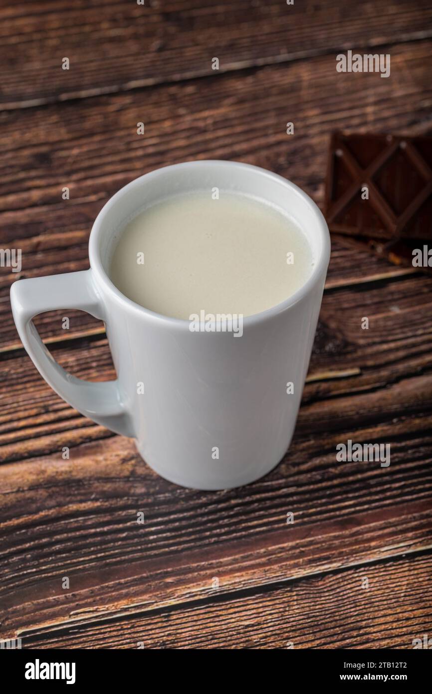 Latte con cioccolato in tazza nera su tavolo di legno Foto Stock