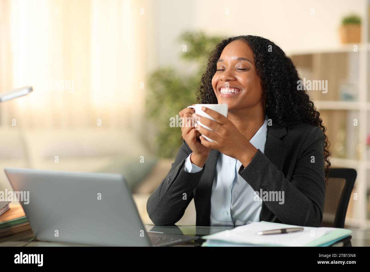 Una donna d'affari nera felice che si prende un caffè e si rilassa a casa Foto Stock