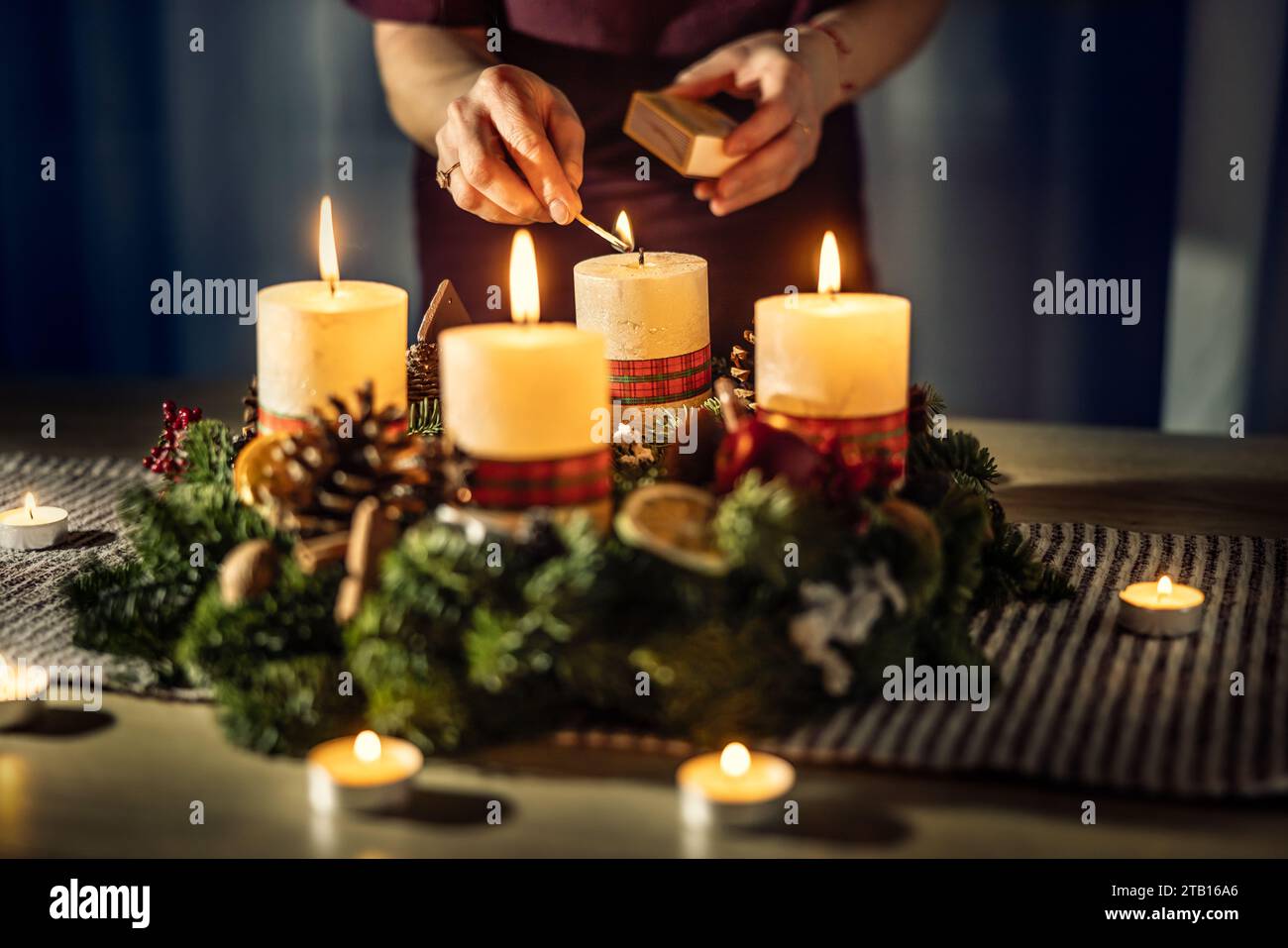 Una donna accende l'ultima quarta candela su una corona d'Avvento durante la vigilia di Natale. Foto Stock
