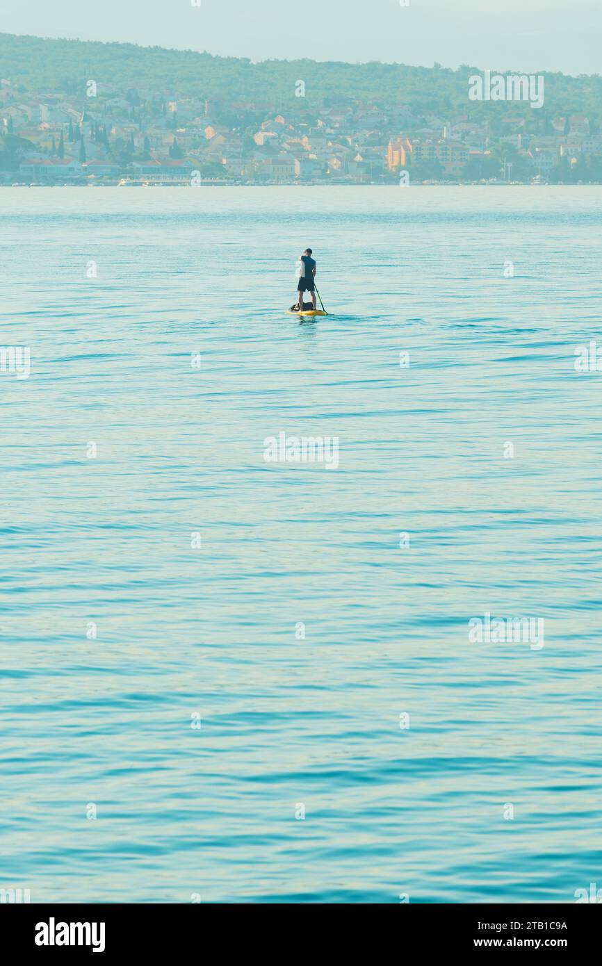 Persona irriconoscibile stand-up paddle boarding nel mare Adriatico Golfo del Quarnero visto dalla costa della città di Crikvenica, attenzione selettiva Foto Stock