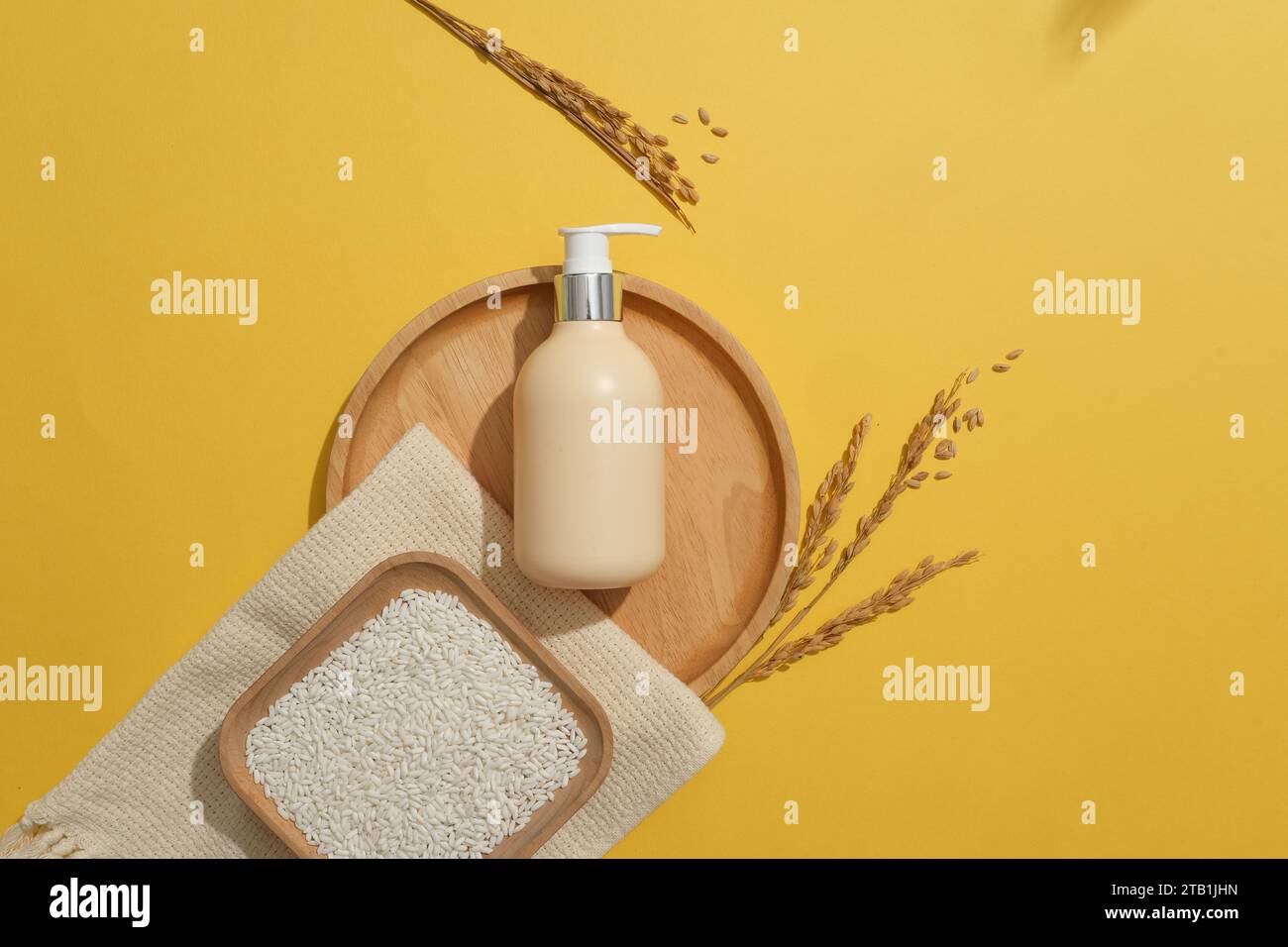 Piatto quadrato di riso posto su una sciarpa. Etichetta vuota della bottiglia della pompa visualizzata su un vassoio di legno su sfondo giallo. Confezione contenitore del marchio Skin Care Foto Stock