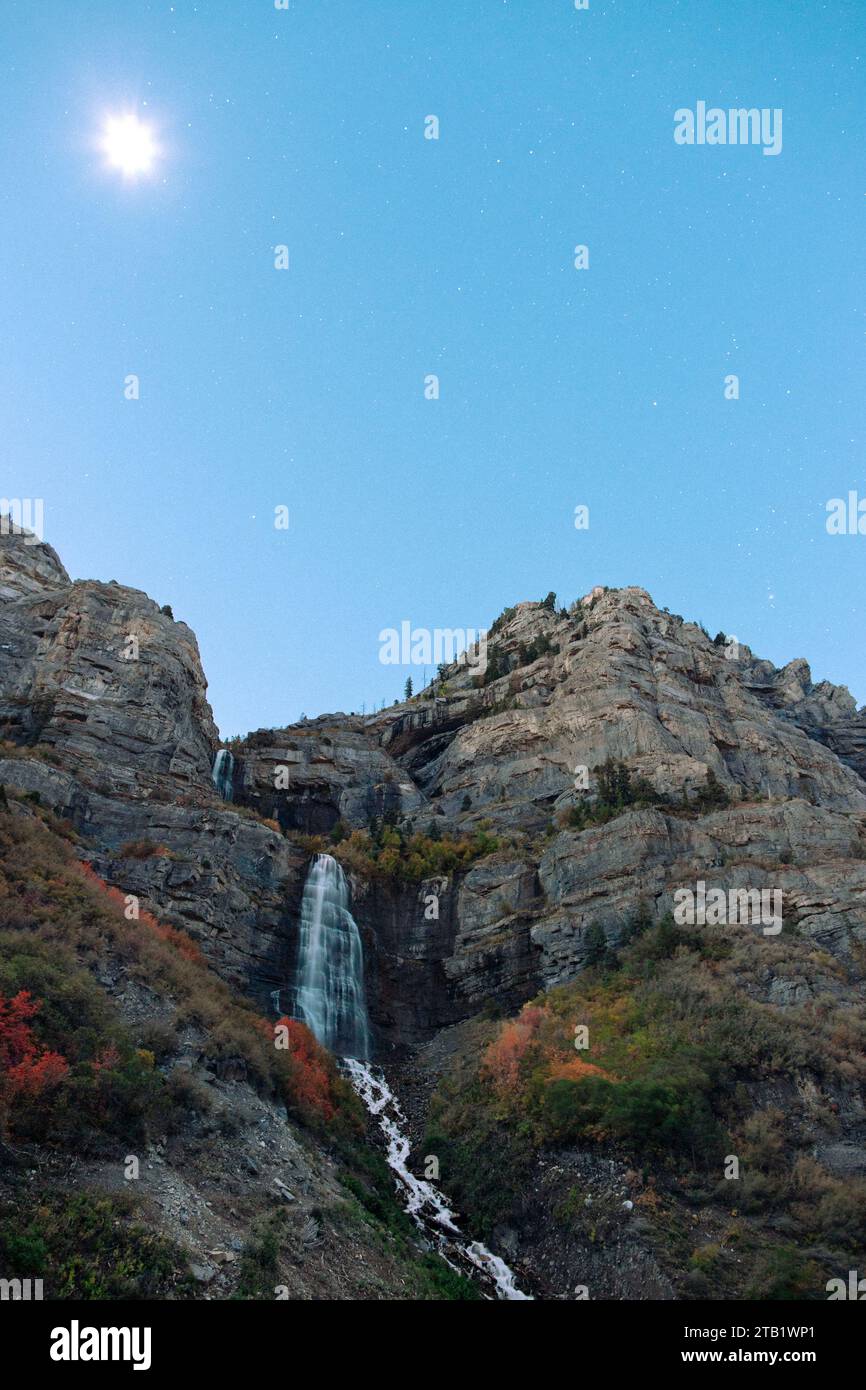 Una cascata corre fuori da un canyon mentre le stelle riempiono il cielo mattutino. Foto Stock