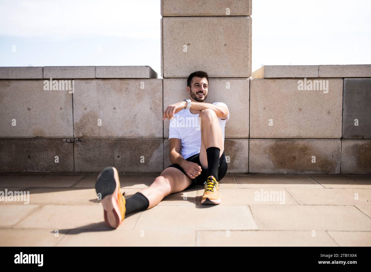 Giovane allegro atleta di corsa maschile che riposa durante l'allenamento sul pavimento Foto Stock