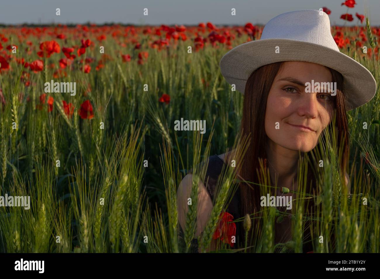Una giovane donna con Un cappello bianco seduta su Un Poppy Field la sera Foto Stock