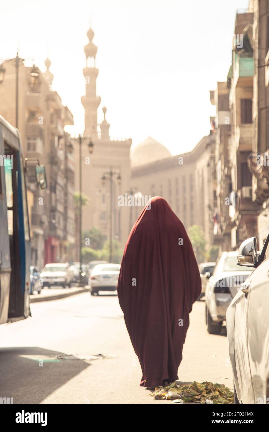 Una donna musulmana, che indossa un burka rosso, cammina per le strade del Cairo Foto Stock