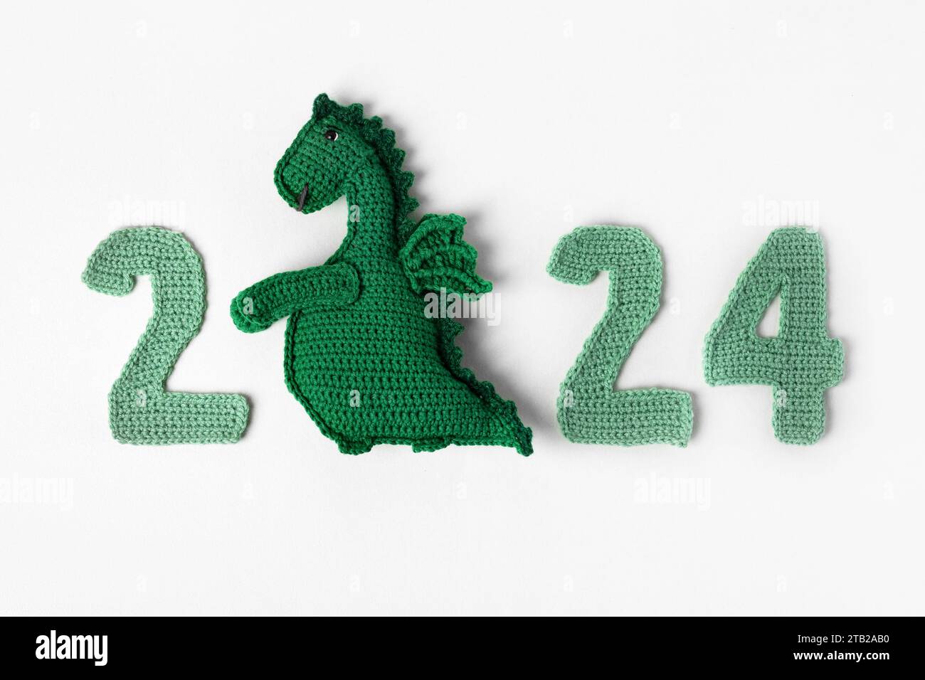 Drago verde giocattolo a maglia e numeri verdi a maglia. Il simbolo dell'anno 2024 su sfondo grigio. Foto Stock