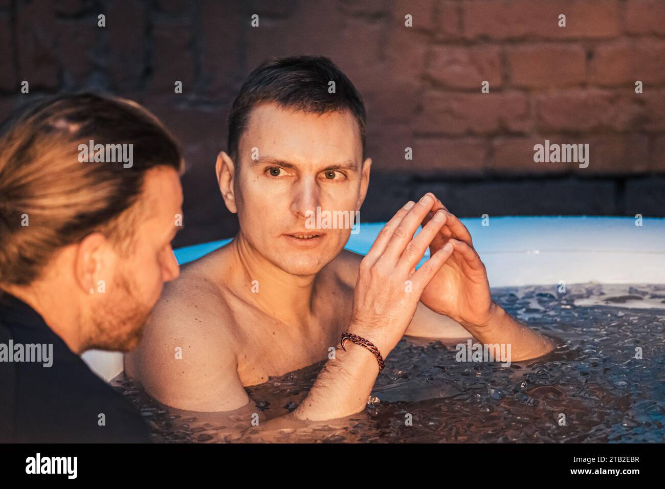 Uomo che fa il bagno di ghiaccio nell'acqua fredda tra cubetti di ghiaccio con istruttore. Metodo Wim Hof, terapia fredda, tecniche respiratorie, yoga, meditazione Foto Stock