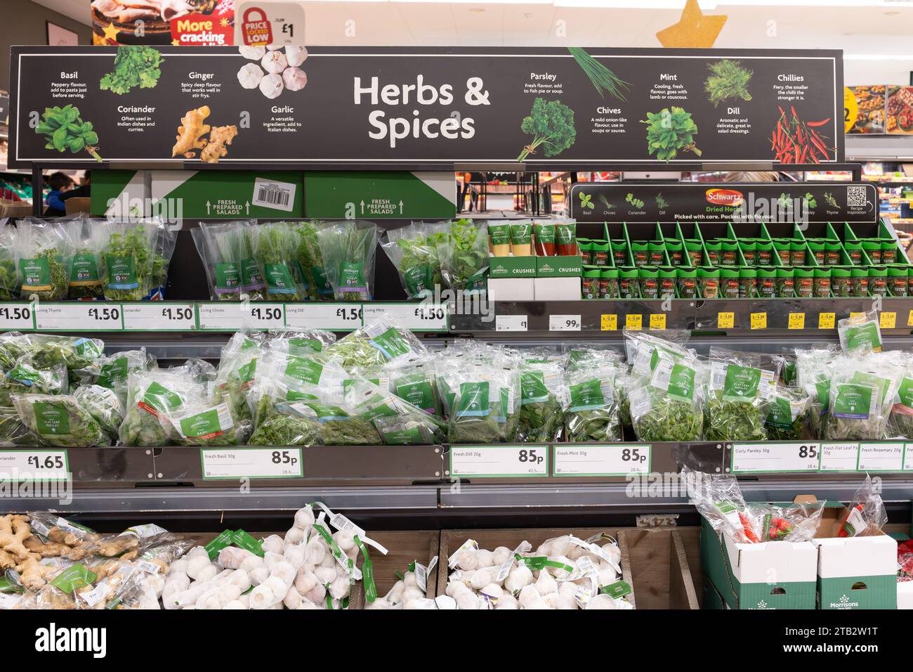 Le erbe e le spezie sono esposte con i prezzi delle erbe fresche in confezioni e vasetti e un cartello pubblicitario sopra in un supermercato Morrisons, Regno Unito Foto Stock