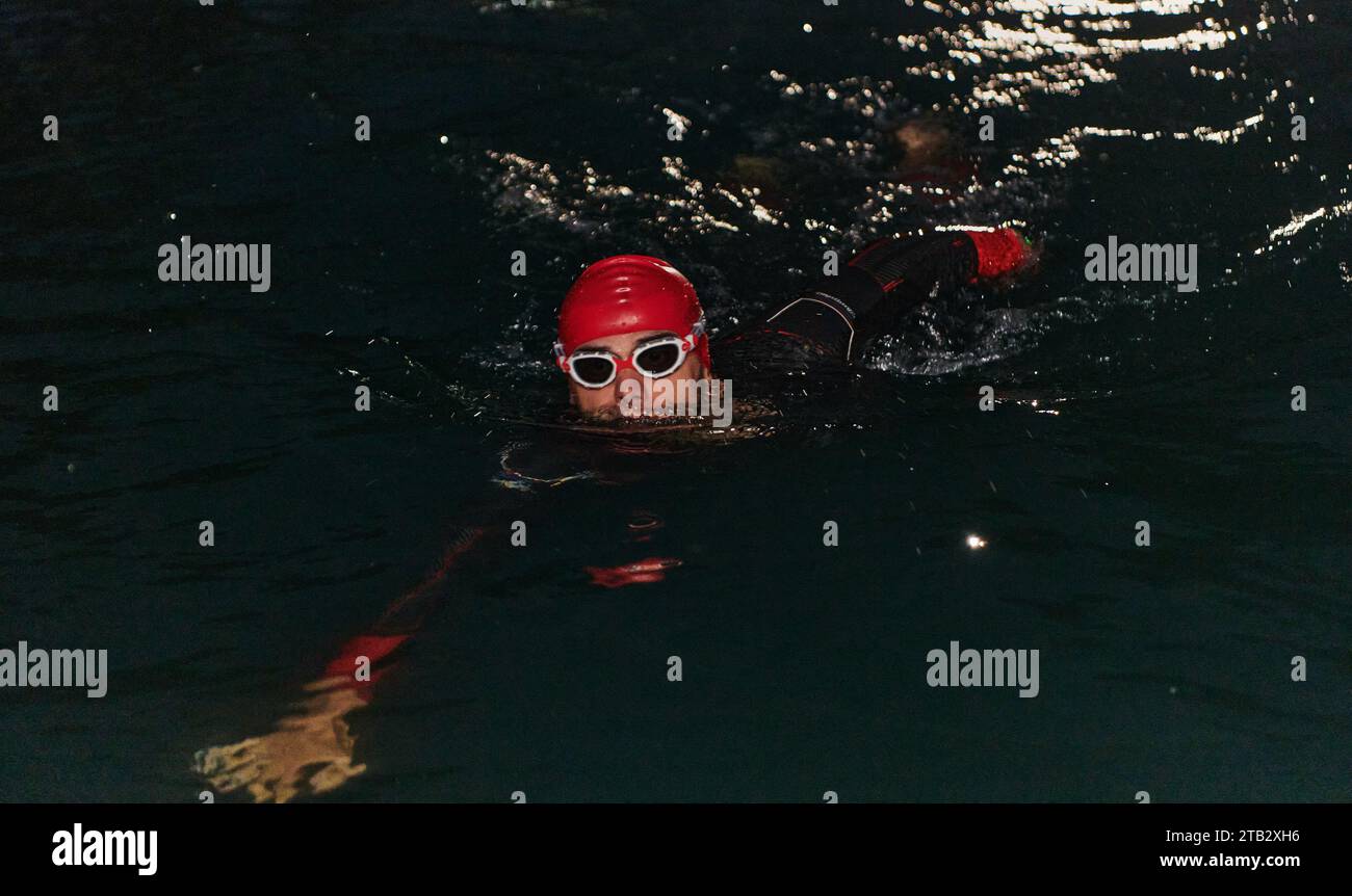 Un triatleta professionista determinato è sottoposto a rigorosi allenamenti notturni in acque fredde, dimostrando dedizione e resilienza in preparazione di un Foto Stock