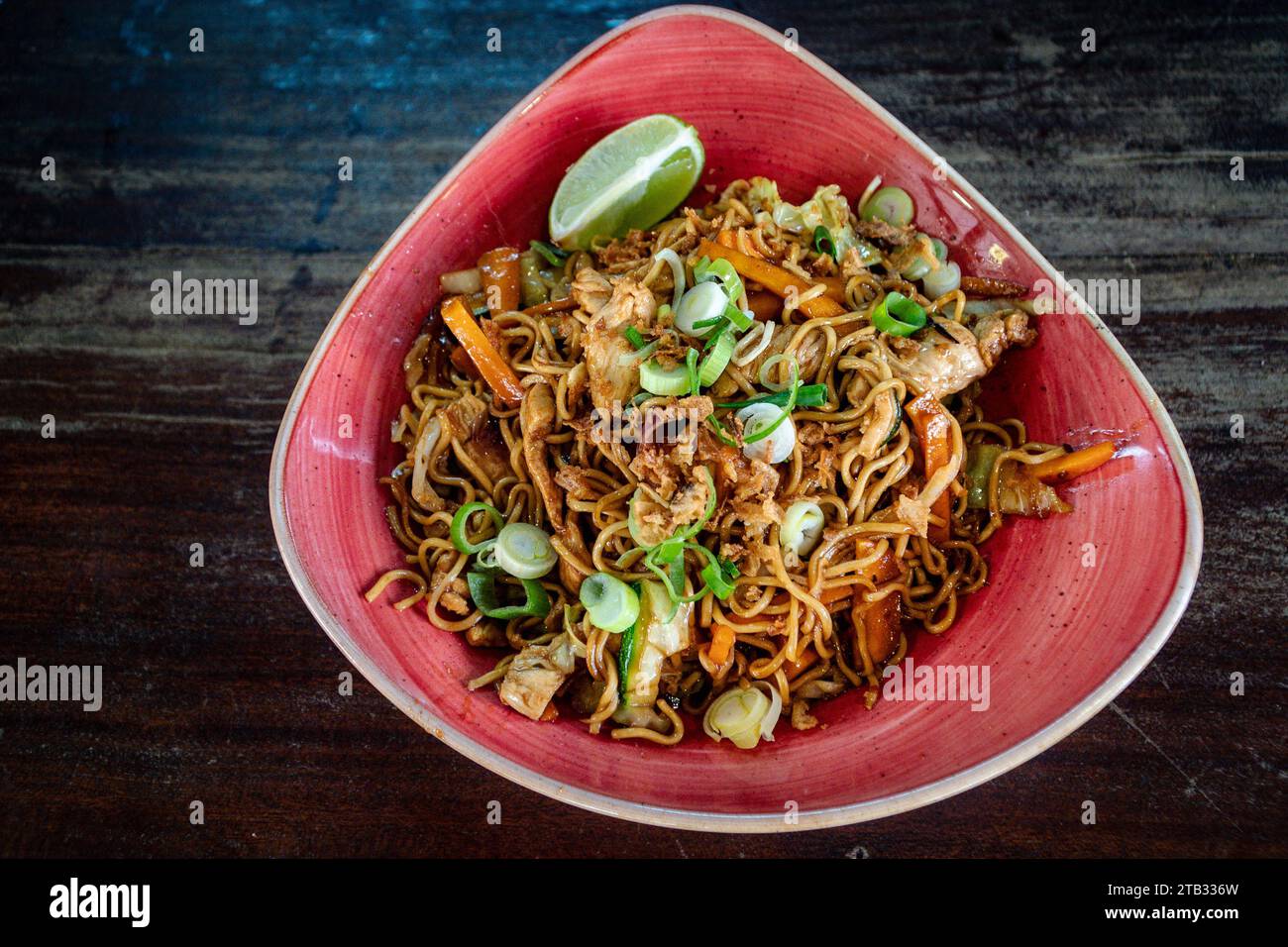 Una ciotola di noodle di pollo e verdure in stile thailandese servita in una ciotola rossa. Foto Stock