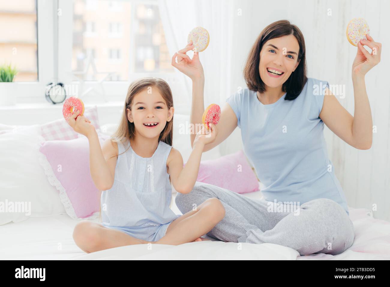 Madre e figlia con le ciambelle, che ridono in una mattinata di sole Foto Stock