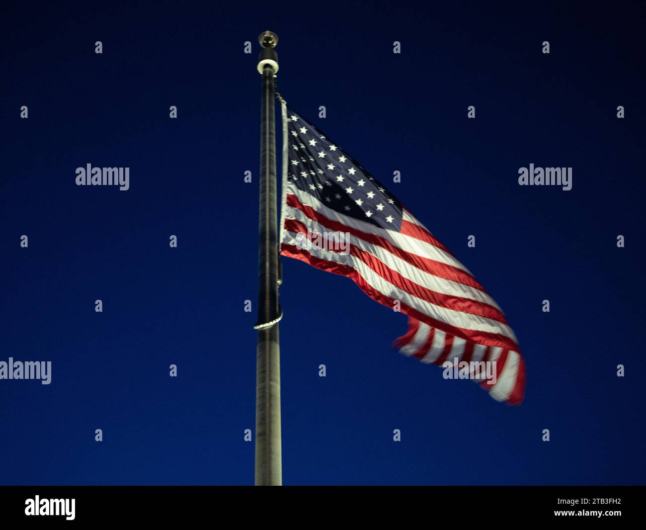 La bandiera degli Stati Uniti d'America, le stelle e le strisce, che soffiano e sventolano nel vento, su un palo della bandiera al crepuscolo Foto Stock