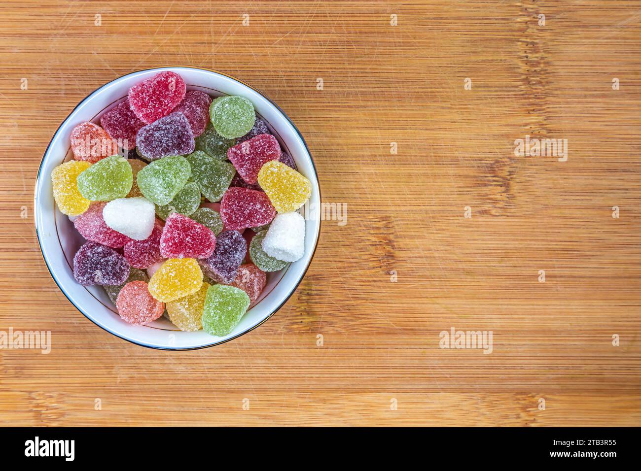 Caramelle di frutta colorate, caramelle gommose in una ciotola di ceramica su un tagliere di legno. Vista dall'alto. Foto Stock