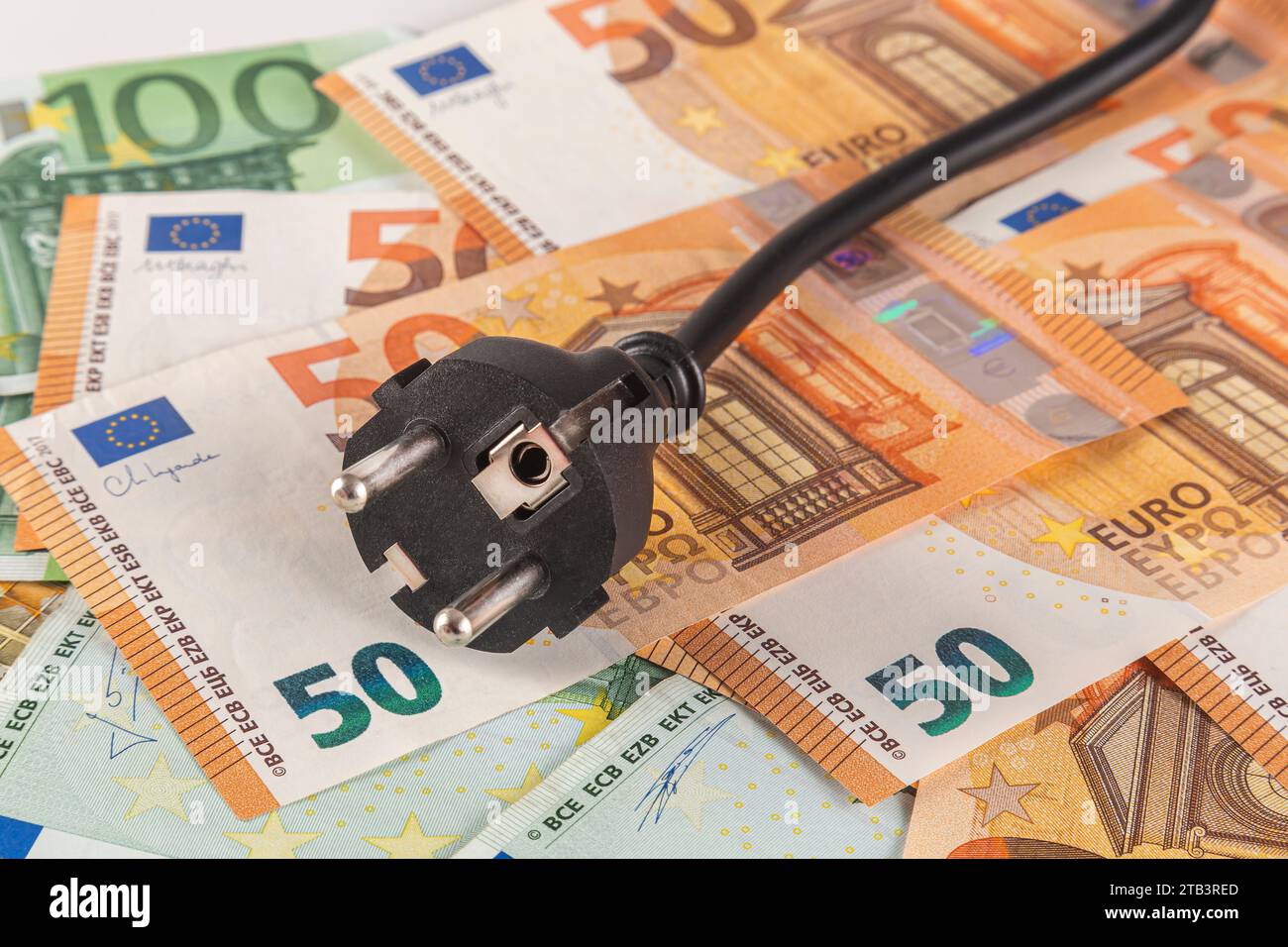 Una spina elettrica nera su un tavolo coperta da un’ampia quantità di banconote in euro su sfondo chiaro da vicino Foto Stock