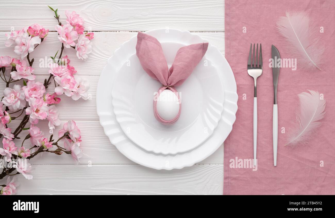Tavolo pasquale festivo con coniglietto in tovagliolo e uovo di lino rosa. Vista dall'alto. Happy Easter Holiday per il menu del ristorante. Svuotare la piastra e. Foto Stock