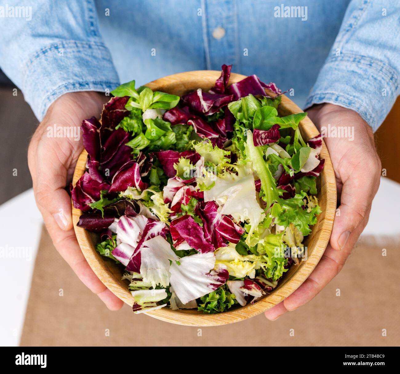 Direttamente sopra la ciotola di bambù con foglie di insalata verde in mani maschili. Mangiare sano. Foto Stock