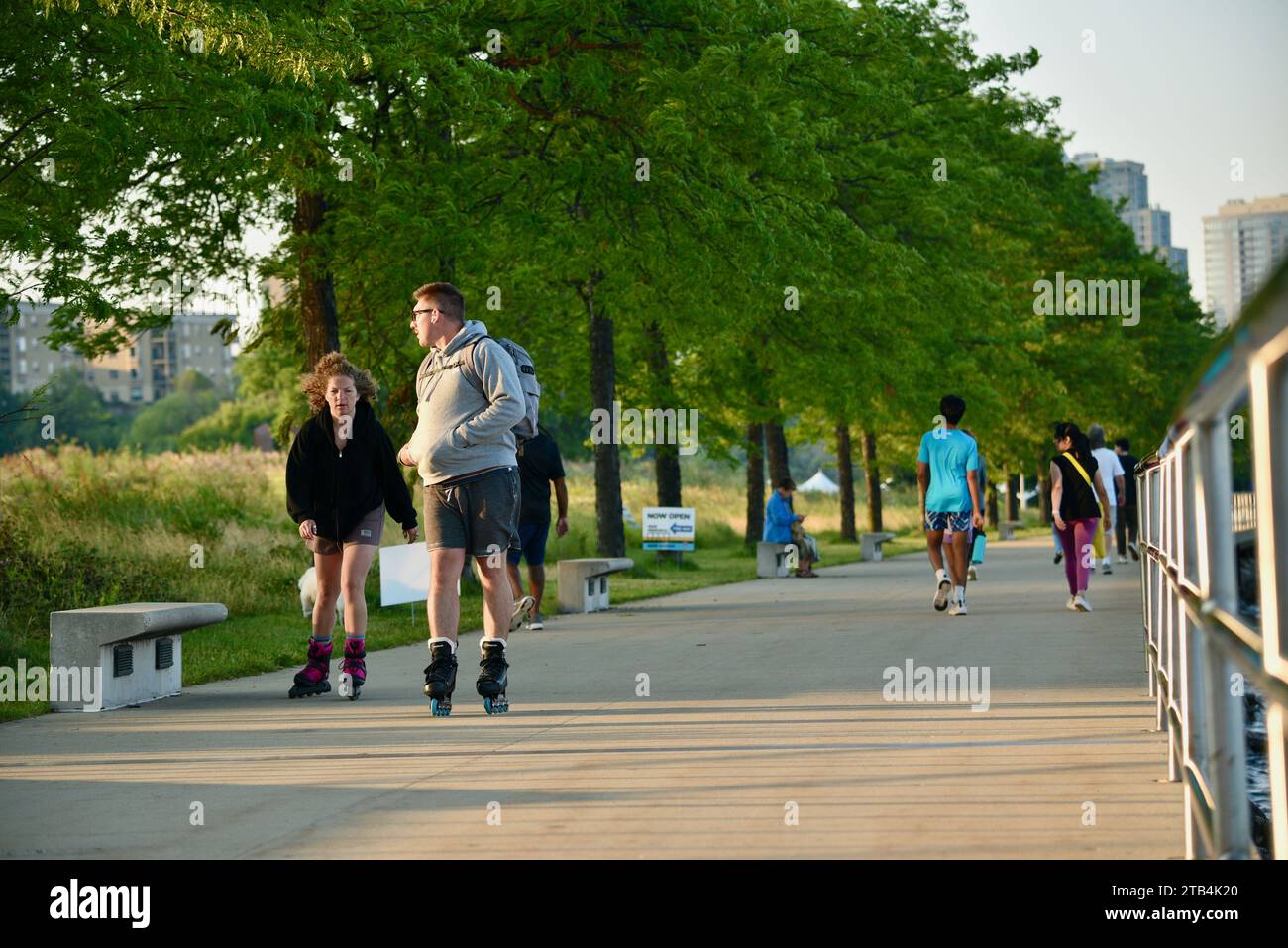 Giovane coppia con pattini e altre persone che camminano o fanno jogging lungo il parco sul lungomare al tramonto nel centro di Milwaukee, Wisconsin, Stati Uniti Foto Stock