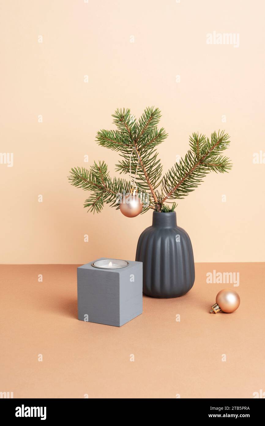 Ramo di abete rosso in vaso di ceramica grigia, candela e pallina di Natale su tavolo beige. Stile natalizio minimalista Foto Stock