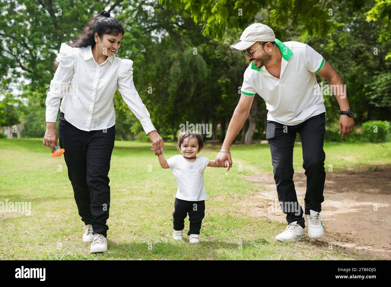 Genitori indiani felici e giovani che tengono per mano la figlia che cammina nel parco o nel giardino. Foto Stock