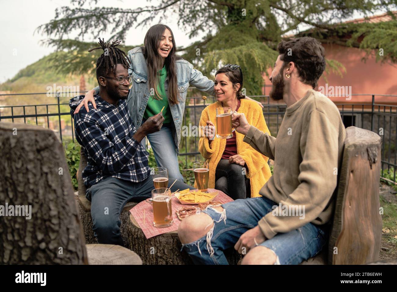 Un gruppo eterogeneo di amici condivide drink e Risate mentre si gode un ritrovo informale in un parco naturale. Foto Stock