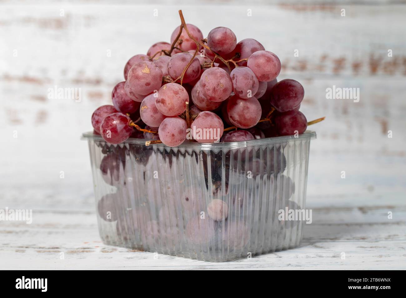 Uva viola confezionata su fondo di legno bianco. Prodotti agricoli biologici. Delizioso mazzo di uva Foto Stock