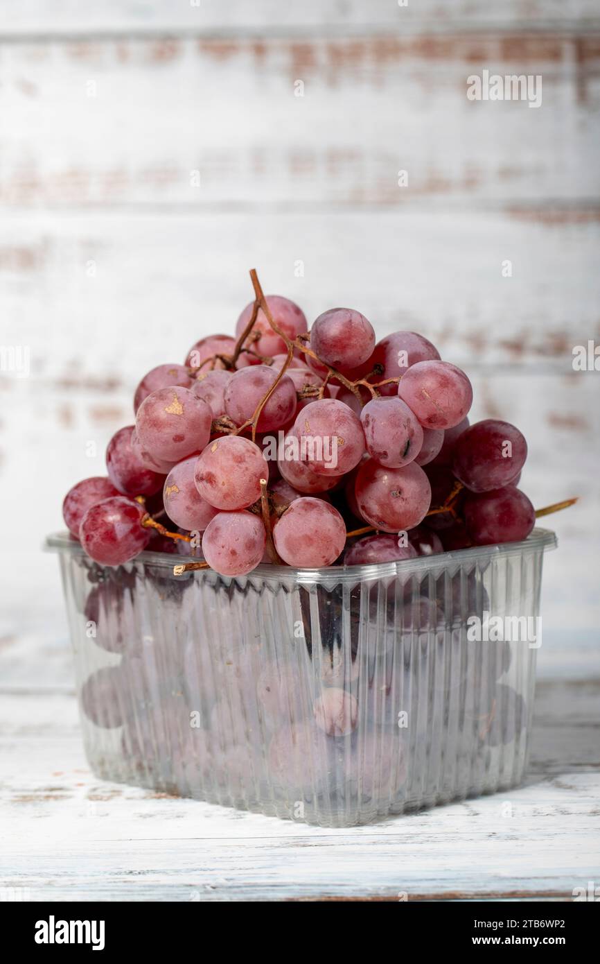 Uva viola confezionata su fondo di legno bianco. Prodotti agricoli biologici. Delizioso mazzo di uva Foto Stock