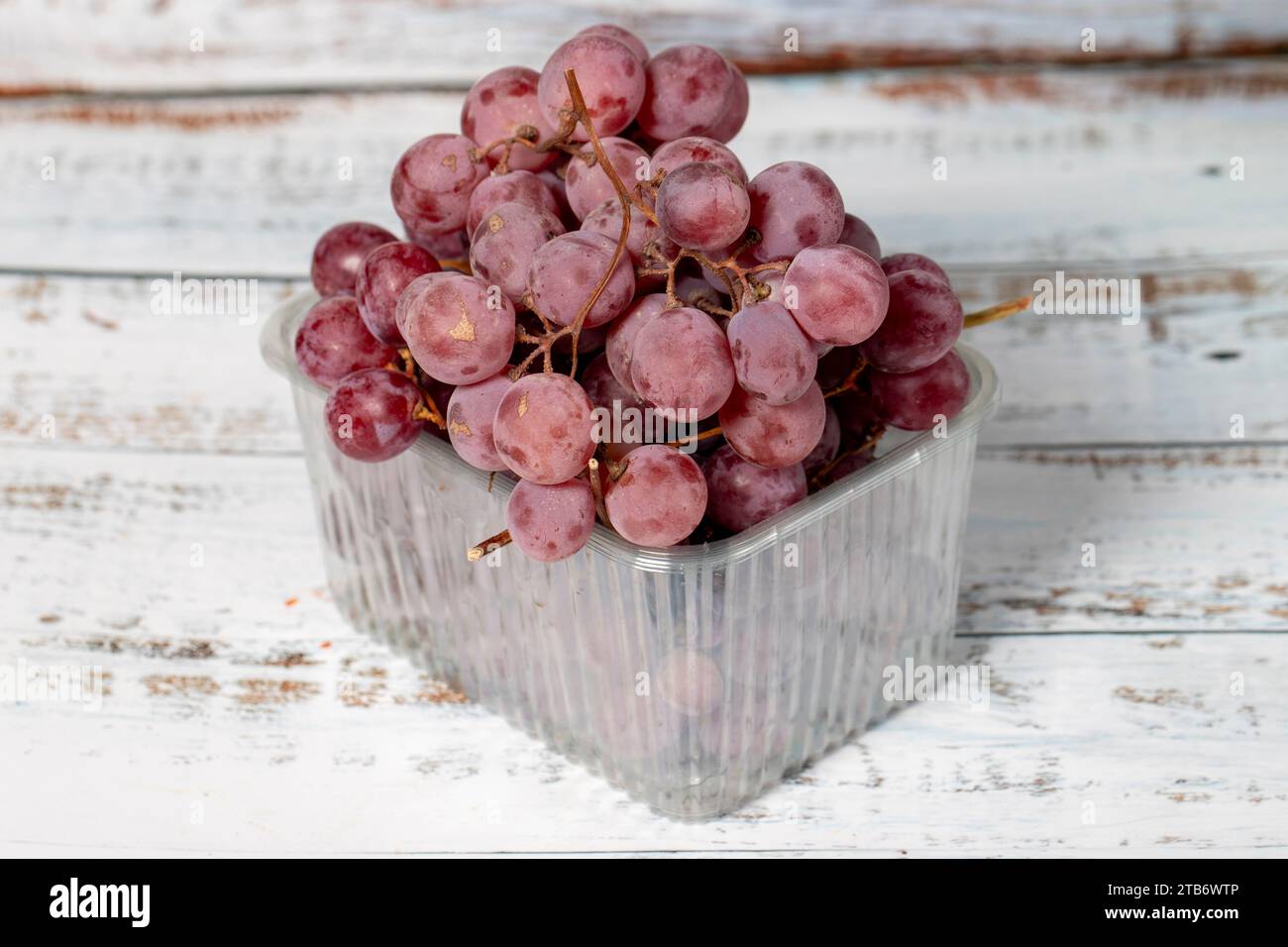 Uva viola confezionata su fondo di legno bianco. Prodotti agricoli biologici. Delizioso mazzo di uva Foto Stock
