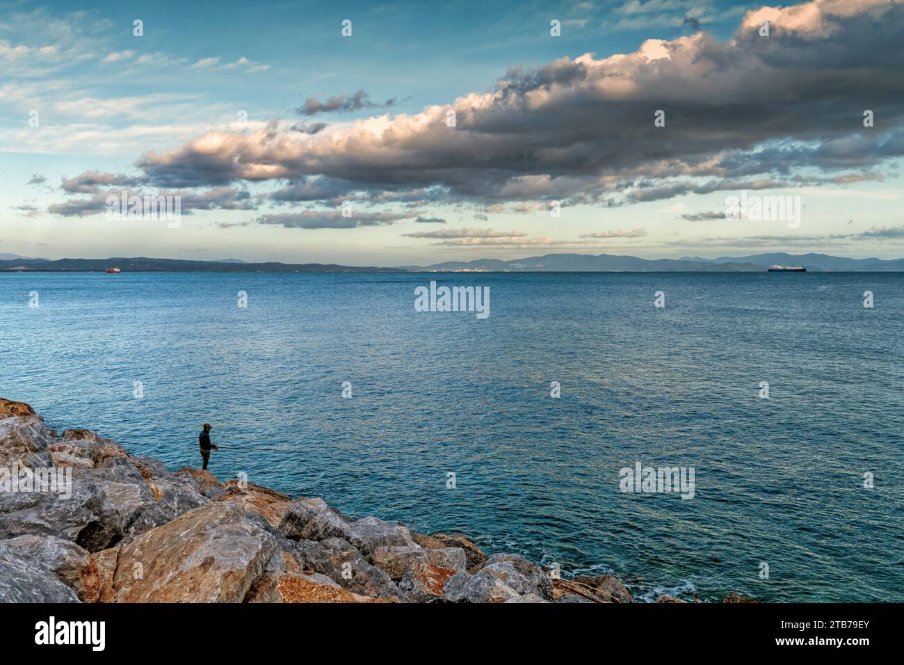 Piombino, Italia - 11 novembre 2023: Pescatore solitario che pesca al largo del molo del porto di Piombino al tramonto Foto Stock