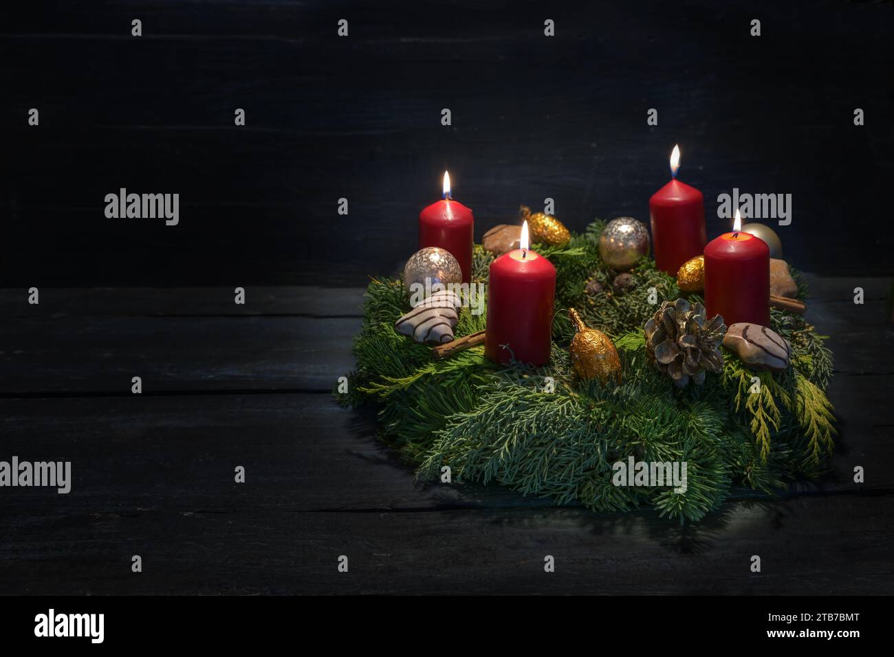 Luce al buio al quarto avvento, corona verde naturale con candele rosse, quattro sono in fiamme, decorazioni natalizie e biscotti, fondo di legno scuro, Foto Stock