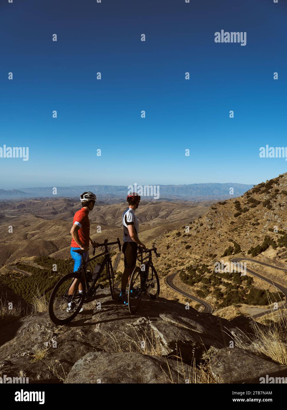 Vista laterale due ciclisti in piedi con le loro mountain bike che si affacciano su una strada tortuosa e colline ondulate Foto Stock