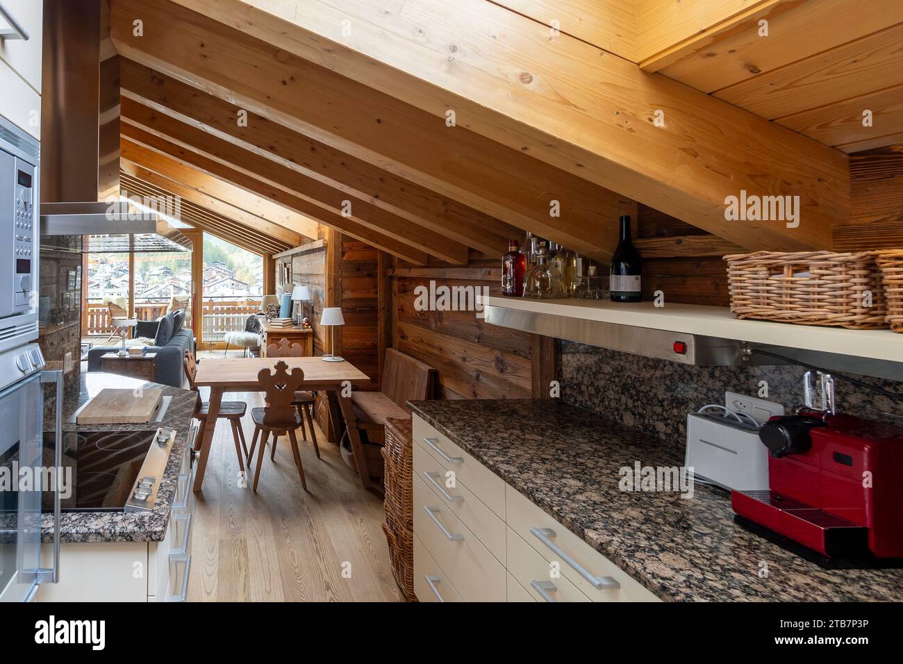 Un caldo e invitante abitacolo in legno caratterizzato da una moderna cucina con elettrodomestici in acciaio inox, ripiani in granito e una spaziosa area pranzo Foto Stock