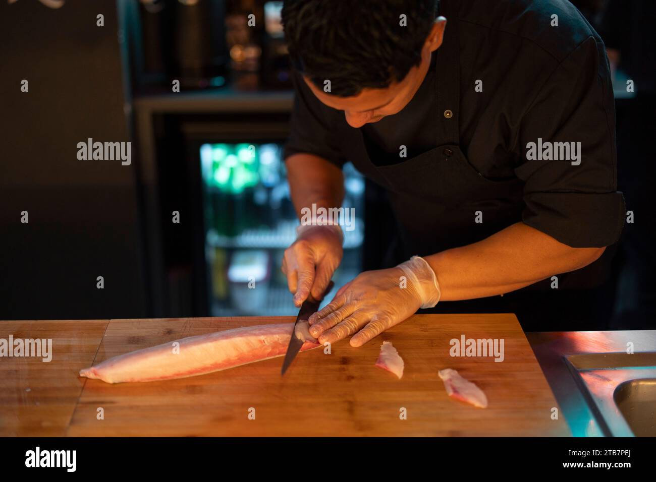 Un esperto sushi chef prepara meticolosamente pesce fresco con precisione, mettendo in mostra l'arte della preparazione del sushi. Foto Stock