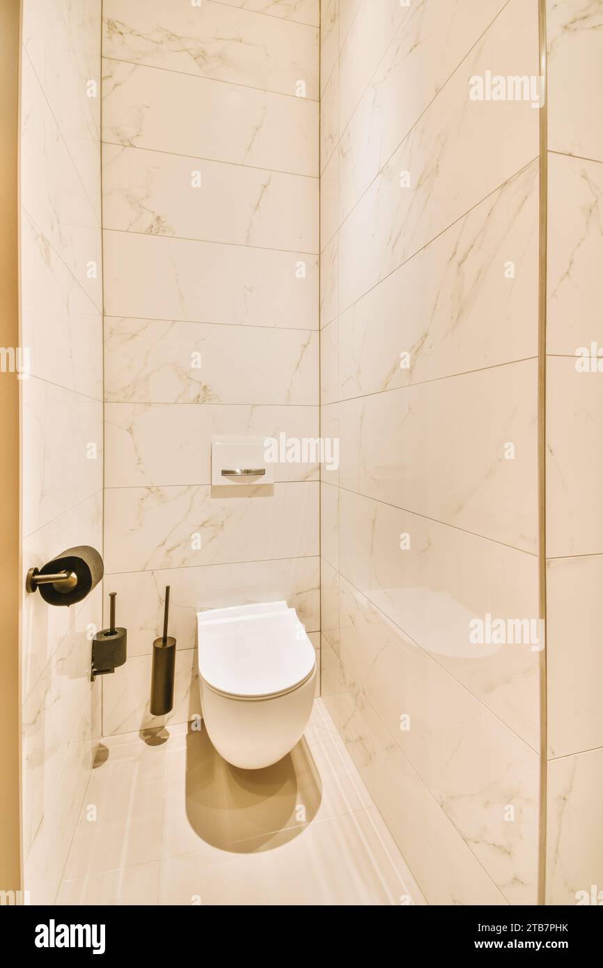 L'interno di un piccolo bagno pulito con ciotola in ceramica circondata da pareti piastrellate bianche in un appartamento moderno Foto Stock