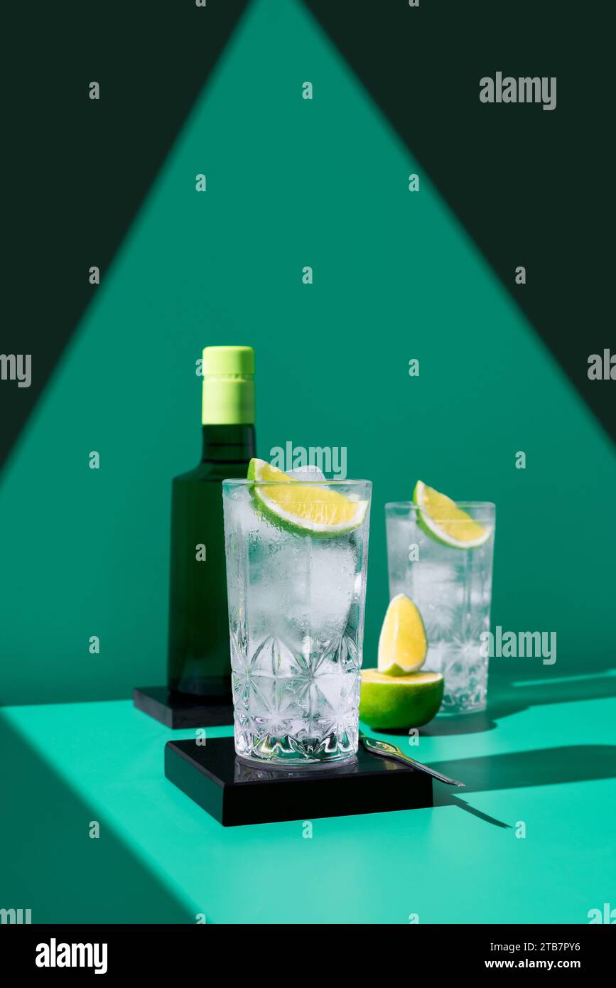 Un elegante gin tonic su uno sfondo geometrico con fette di lime vibranti che proiettano ombre morbide. Foto Stock