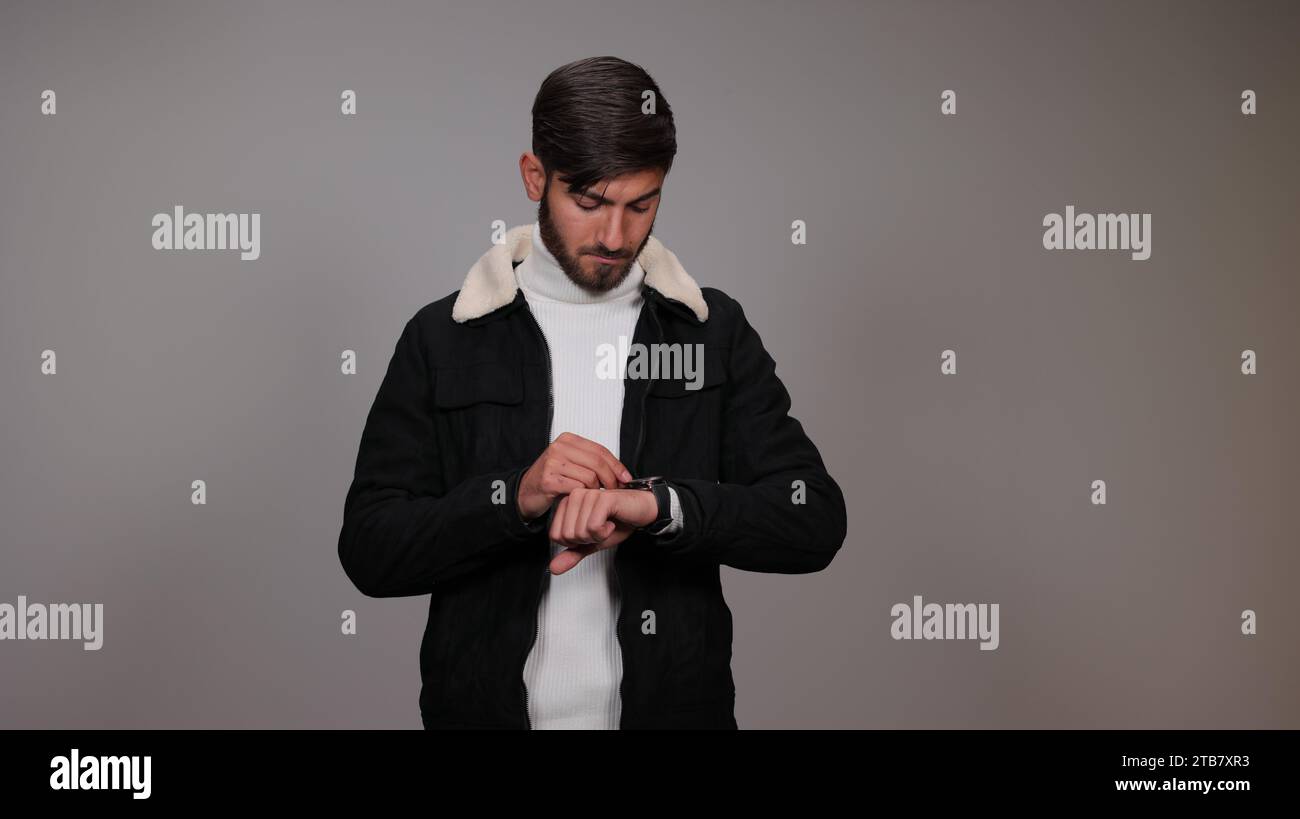 Un giovane che controlla l'ora sul suo orologio da polso su uno sfondo grigio. Foto Stock