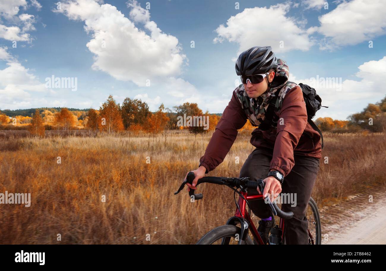 Il ciclista fa un giro in bicicletta su un sentiero nel campo. Uomo in casco e occhiali in bicicletta all'aperto. Foto Stock
