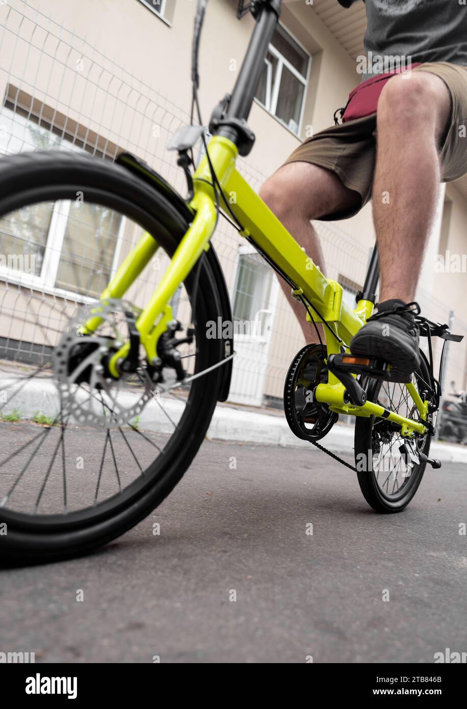 Visuale dall'angolo basso dell'uomo che guida una bicicletta pieghevole compatta per gli spostamenti in città. Foto Stock