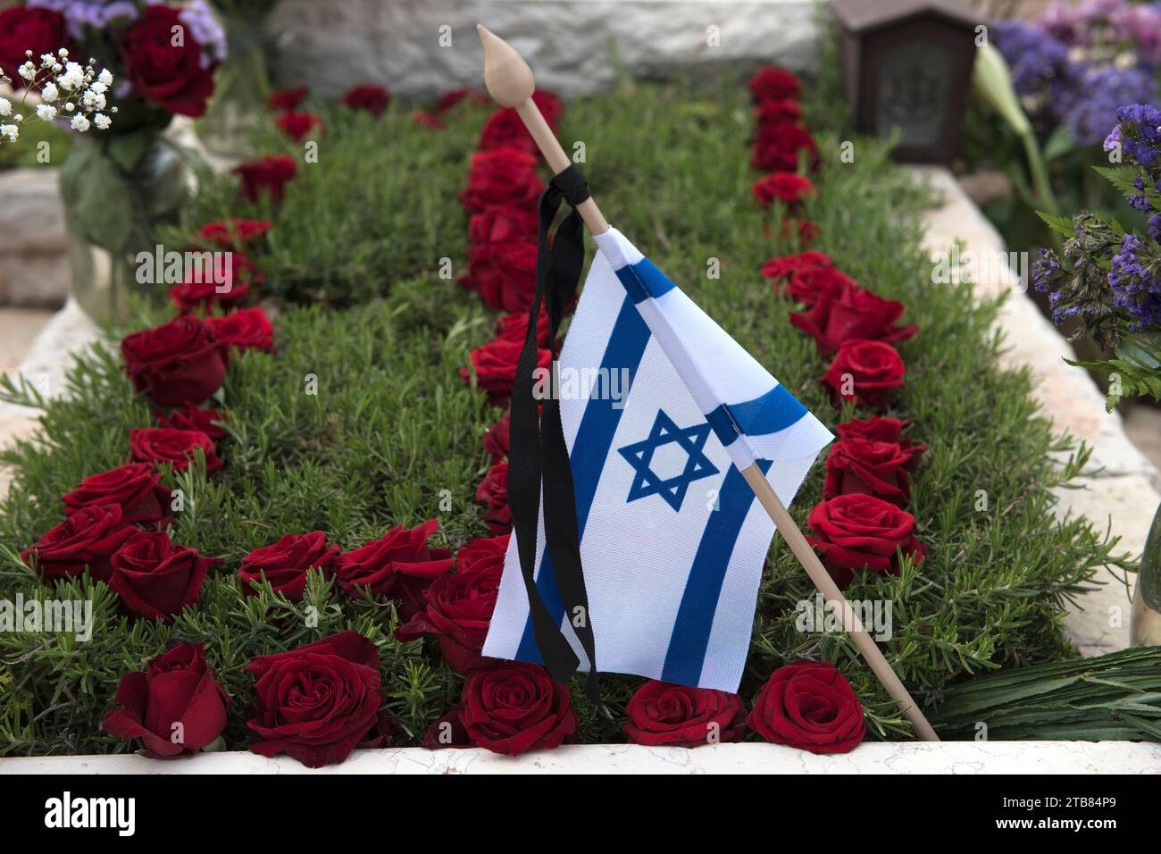 Una bandiera dello Stato di Israele poggia su una tomba di un soldato caduto coperto di fiori colorati nel cimitero militare di Har Herzl a Gerusalemme Foto Stock